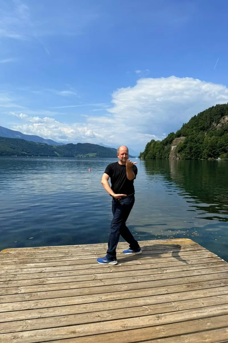 Christian Weidl in einer Qi-Gong-Haltung am Seeufer — ruhiger Stand, konzentrierter Atem